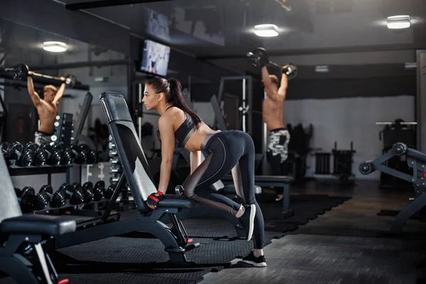 İnce vücut geliştirmeci kız ve erkek spor salonunda bir egzersiz sırasında aynanın önünde duran bir ağır halter kaldırma. Spor kavramı, yağ yakma ve sağlıklı yaşam tarzı.