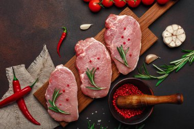Çiğ domuz biftek domates, biberiye, sarımsak, biber, tuz ve baharat harç paslı kahverengi zemin üzerine ile kesme tahtası üzerinde parçaları. Üstten görünüm.