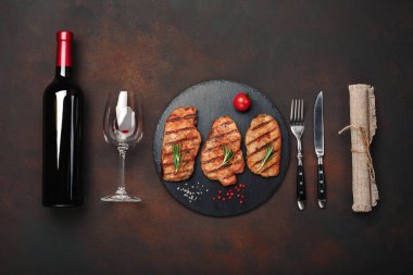 Taş ile şişe şarap, şarap kadehi, bıçak ve çatal paslı arka plan üzerinde ızgara domuz biftek. Üstten görünüm.