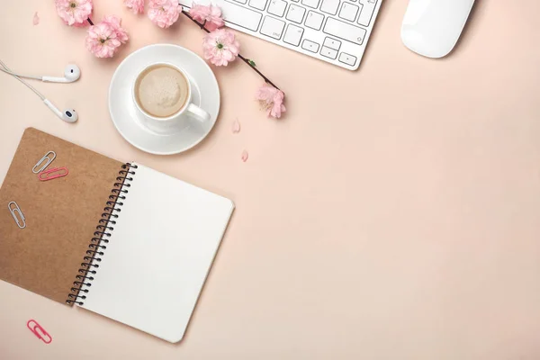 Beyaz fincan kapuçino, sakura çiçekler, klavye, çalar saat, defter üzerinde pastel pembe arka plan ile. Metin alanı olan üstten görünüm.
