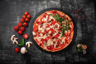 Pizza Tütsülenmiş sosis, peynir, mantar, domates, biber ve yeşillik bir taş ve bir siyah tebeşir tahtası, üstten görünüm.