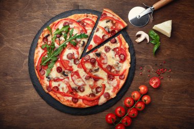 Pizza Tütsülenmiş sosis, peynir, mantar, cherry domates, biber ve yeşillik bir taş ve ahşap kahverengi masa, üstten görünüm.