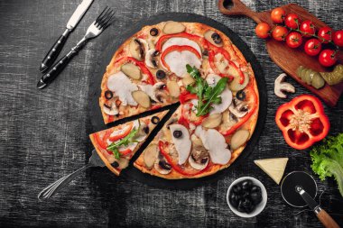 Peynir, jambon, salatalık turşusu, et ve bir taş ve bir siyah tebeşir tahtası, üstten görünüm zeytin pizza.