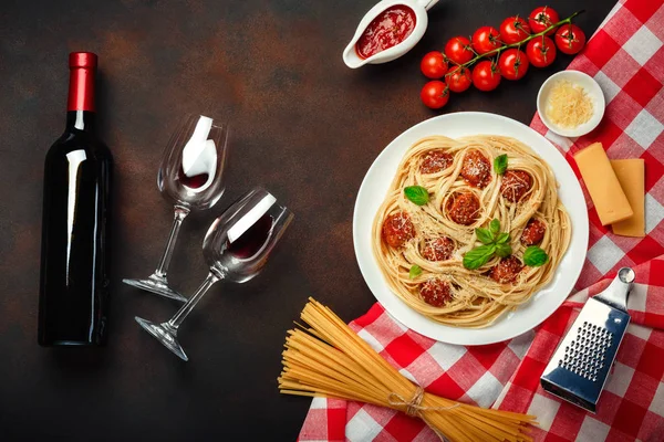 Spaghetti pasta with meatballs, cherry tomato sauce, cheese, wineglass and bottle on rusty background, top view.