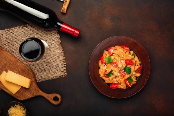 Pasta with cheese, cherry tomato sauce, wineglass and bottle wine on rusty background, top view