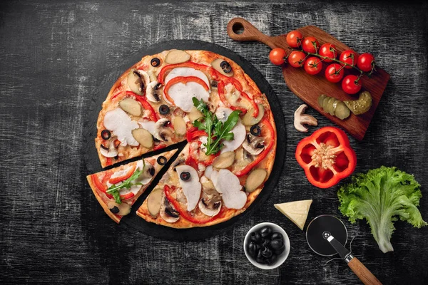 Peynir, jambon, salatalık turşusu, et ve bir taş ve bir siyah tebeşir tahtası, üstten görünüm zeytin pizza.