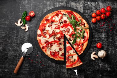 Bir dilim pizza bir spatula Tütsülenmiş sosis, peynir, mantar, domates, biber ve yeşillik bir taş ve bir siyah tebeşir tahtası üzerinde.