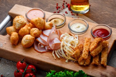 Aperatifler bira o katmak için büyük kümesi kızarmış peynir topları, helezon peynir, jambon ve yengeç sopa hizmet sarımsak soslar, ketçap ve hardal bir ahşap tahta ve kahverengi zemin üzerinde.