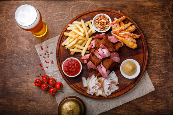 Big set of snacks for beer or alcohol and it includes smoked pork meat, french fries, fried bread, crab sticks and nuts served with sauces on a wooden background. Top view.