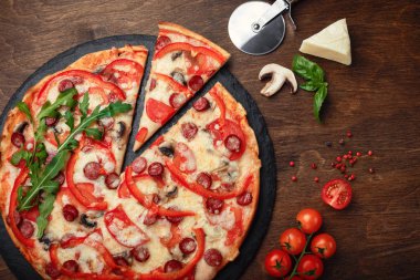 Pizza Tütsülenmiş sosis, peynir, mantar, cherry domates, biber ve yeşillik bir taş ve ahşap kahverengi masa, üstten görünüm.