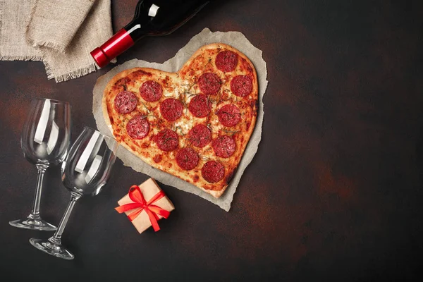 Pizza mozzarella peyniri, sausagered, şarap şişesi, iki bardağı, hediye kutusu paslı arka plan üzerinde kalp şeklinde. Üstten görünüm.