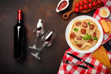 Spagetti makarna köfte, kiraz domates sosu, peynir, bardağı ve şişe paslı arka planda, üstten görünüm.