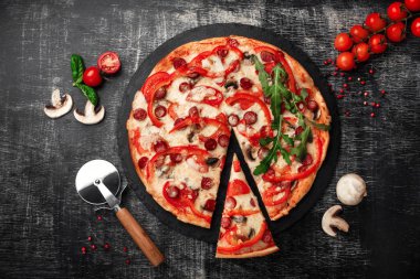 Bir dilim pizza bir spatula Tütsülenmiş sosis, peynir, mantar, domates, biber ve yeşillik bir taş ve bir siyah tebeşir tahtası üzerinde.