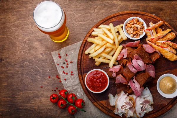 Big set of snacks for beer or alcohol and it includes smoked pork meat, french fries, fried bread, crab sticks and nuts served with sauces on a wooden background. Top view.