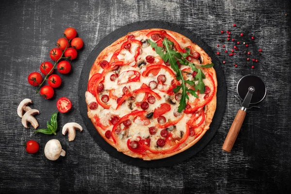 Pizza Tütsülenmiş sosis, peynir, mantar, domates, biber ve yeşillik bir taş ve bir siyah tebeşir tahtası, üstten görünüm.