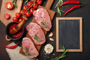 Çiğ domuz biftek domates, biberiye, sarımsak, biber, tuz ve baharat harç ve tebeşir tahtaya paslı kahverengi zemin ile kesme tahtası üzerinde parçaları. Metin alanı olan üstten görünüm.