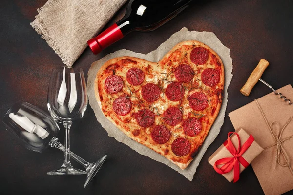 Pizza mozzarella peyniri, sausagered, şarap şişesi, iki bardağı, hediye kutusu paslı arka plan üzerinde kalp şeklinde. Üstten görünüm.