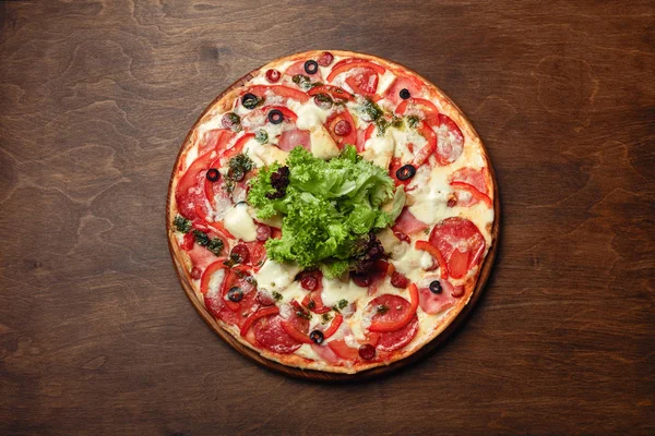 Pizza jambon, salam, peynir, mantar, domates, biber ve salata ahşap kahverengi tahtası, üstten görünüm.