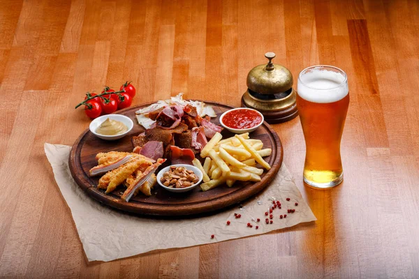 Big set of snacks for beer or alcohol and it includes smoked pork meat, french fries, fried bread, crab sticks and nuts served with sauces on a wooden background.