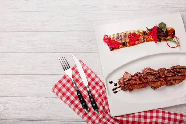 Roasted meat with pineapple in balsamic sauce on a white wooden board, top view.