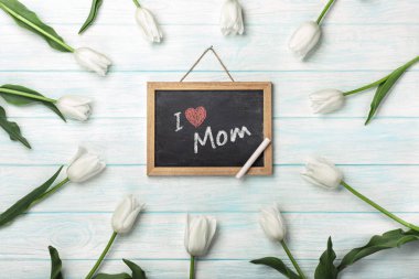 White tulips with chalk board on blue wooden boards. Top view with place for your congratulations. Mother's day.