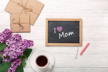 A bouquet of lilacs with cup of tea, chalk board, craft envelope, a love note on rusty background. Top view with place for your text. Mother's day.