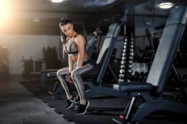 Slim, bodybuilder girl, lifts heavy dumbbell standing in front of the mirror while training in the gym. Sports concept, fat burning and a healthy lifestyle.