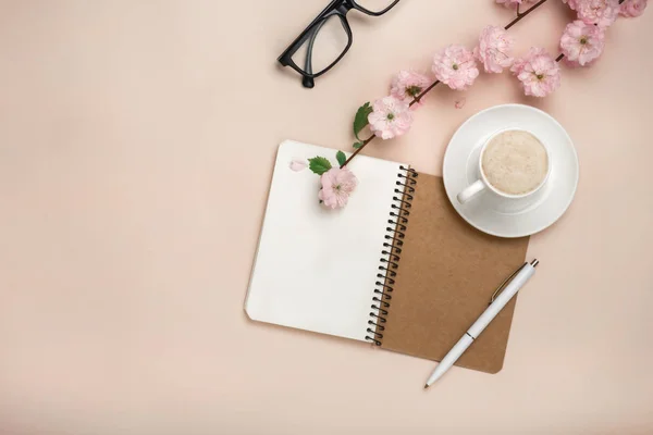 Beyaz fincan kapuçino, sakura çiçekler, defter üzerinde pastel pembe arka plan ile. Metin alanı olan üstten görünüm.