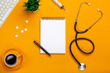 Tablonun bir doktorun not defteri ve kalem stetoskop, klavye, reçete ve ilaç, bir fincan kahve senin metin için yer ile sarı bir arka plan üzerinde üstten görünüm.