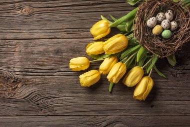 Sarı laleler bir kağıt torba, bir ahşap arka plan üzerinde bir yuva ile Paskalya yumurta. Kopya alanı ile üstten görünüm