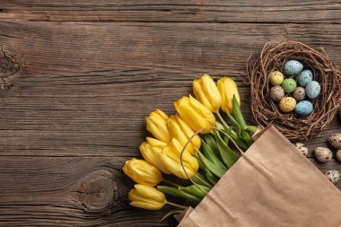 Sarı laleler bir kağıt torba, bir ahşap arka plan üzerinde bir yuva ile Paskalya yumurta. Kopya alanı ile üstten görünüm