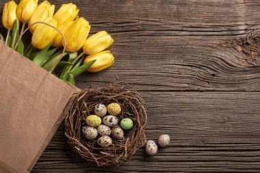 Sarı laleler bir kağıt torba, bir ahşap arka plan üzerinde bir yuva ile Paskalya yumurta. Kopya alanı ile üstten görünüm