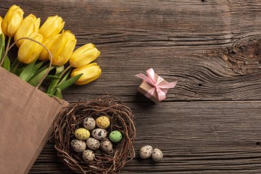 Sarı laleler bir kağıt torba, bir ahşap arka plan üzerinde bir yuva ile Paskalya yumurta. Kopya alanı ile üstten görünüm