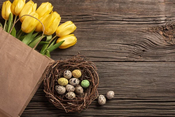 Sarı laleler bir kağıt torba, bir ahşap arka plan üzerinde bir yuva ile Paskalya yumurta. Kopya alanı ile üstten görünüm
