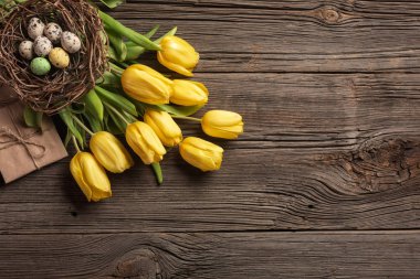 Sarı laleler bir kağıt torba, bir ahşap arka plan üzerinde bir yuva ile Paskalya yumurta. Kopya alanı ile üstten görünüm.
