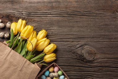 Sarı laleler bir kağıt torba, bir ahşap arka plan üzerinde bir yuva ile Paskalya yumurta. Kopya alanı ile üstten görünüm.
