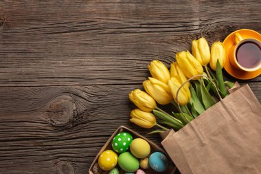 Sarı laleler bir kağıt torba, bir ahşap arka plan üzerinde bir yuva ile Paskalya yumurta. Kopya alanı ile üstten görünüm.