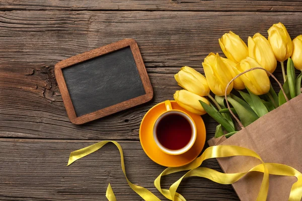 Sarı laleler, ahşap bir arka plan üzerine bir fincan çay ve Paskalya yumurta. Kopya alanı ile üstten görünüm.