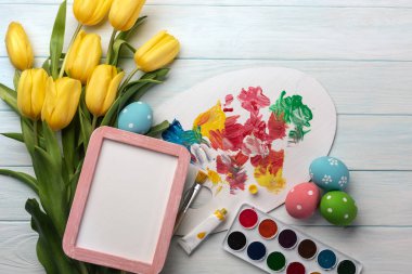Paskalya renkli yumurta, boyalar, fırçalar ve ahşap masa üzerinde Sarı laleler arka plan. Kopya alanı ile Üstten Görünüm