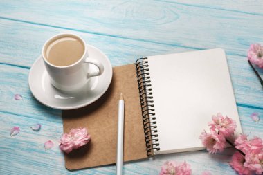 Sakura çiçekli beyaz fincan kapuçino mavi ahşap bir masa üstünde defter. Metin alanı olan üstten görünüm.