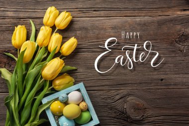 Sarı laleler bir kağıt torba, bir ahşap arka plan üzerinde bir yuva ile Paskalya yumurta. Kopya alanı ile üstten görünüm.