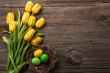 Sarı laleler bir kağıt torba, bir ahşap arka plan üzerinde bir yuva ile Paskalya yumurta. Kopya alanı ile üstten görünüm.