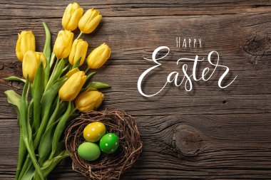 Sarı laleler bir kağıt torba, bir ahşap arka plan üzerinde bir yuva ile Paskalya yumurta. Kopya alanı ile üstten görünüm.