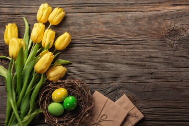 Sarı laleler bir kağıt torba, bir ahşap arka plan üzerinde bir yuva ile Paskalya yumurta. Kopya alanı ile üstten görünüm.
