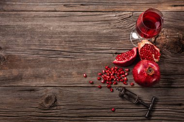 Olgun nar meyve ile bir kadeh şarap ve bir tirbuşon ahşap arka plan üzerinde. Kopya alanı ile üstten görünüm.