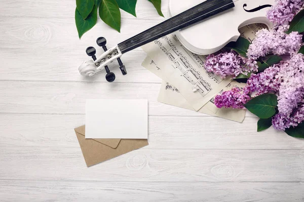 A bouquet of lilacs with violin, letter and music sheet on a white wooden table. Top wiev with space for your text.