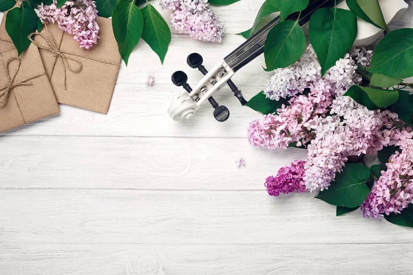 A bouquet of lilacs with violin, letter and music sheet on a white wooden table. Top wiev with space for your text.