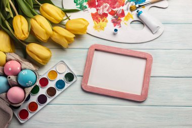 Renkli Paskalya yumurtaları, palet, fırçalar ve beyaz ahşap masa üzerinde sarı laleler boya. Kopya alanı ile üstten görünüm.