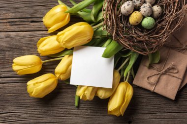 Sarı laleler bir kağıt torba, bir ahşap arka plan üzerinde bir yuva ile Paskalya yumurta. Kopya alanı ile üstten görünüm.