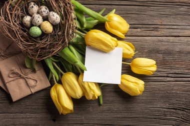 Sarı laleler bir kağıt torba, bir ahşap arka plan üzerinde bir yuva ile Paskalya yumurta. Kopya alanı ile üstten görünüm.